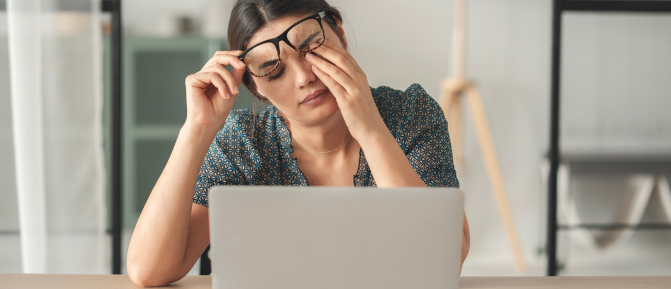 Donna davanti al computer che si massaggia gli occhi affaticati, segno di stanchezza visiva dovuta all’uso prolungato degli schermi.
