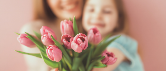 Bambina che regala un mazzo di tulipani rosa alla mamma, simbolo di affetto e Festa della Mamma