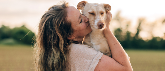 Ragazza che abbraccia e bacia il proprio cane, immagine dedicata alla Giornata Mondiale del Cane e alla cura del suo benessere.