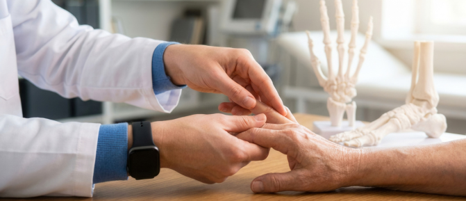 Professionista sanitario che esamina la mano di una persona anziana, con un modello anatomico dello scheletro della mano sullo sfondo, a rappresentare la prevenzione dell'Osteoporosi e la salute delle ossa