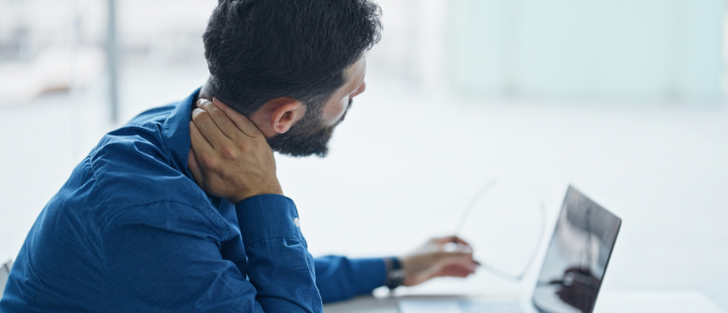 Uomo seduto davanti al computer che si tocca il collo per un fastidio cervicale, a rappresentare tensione e rigidità muscolare legate ai primi freddi